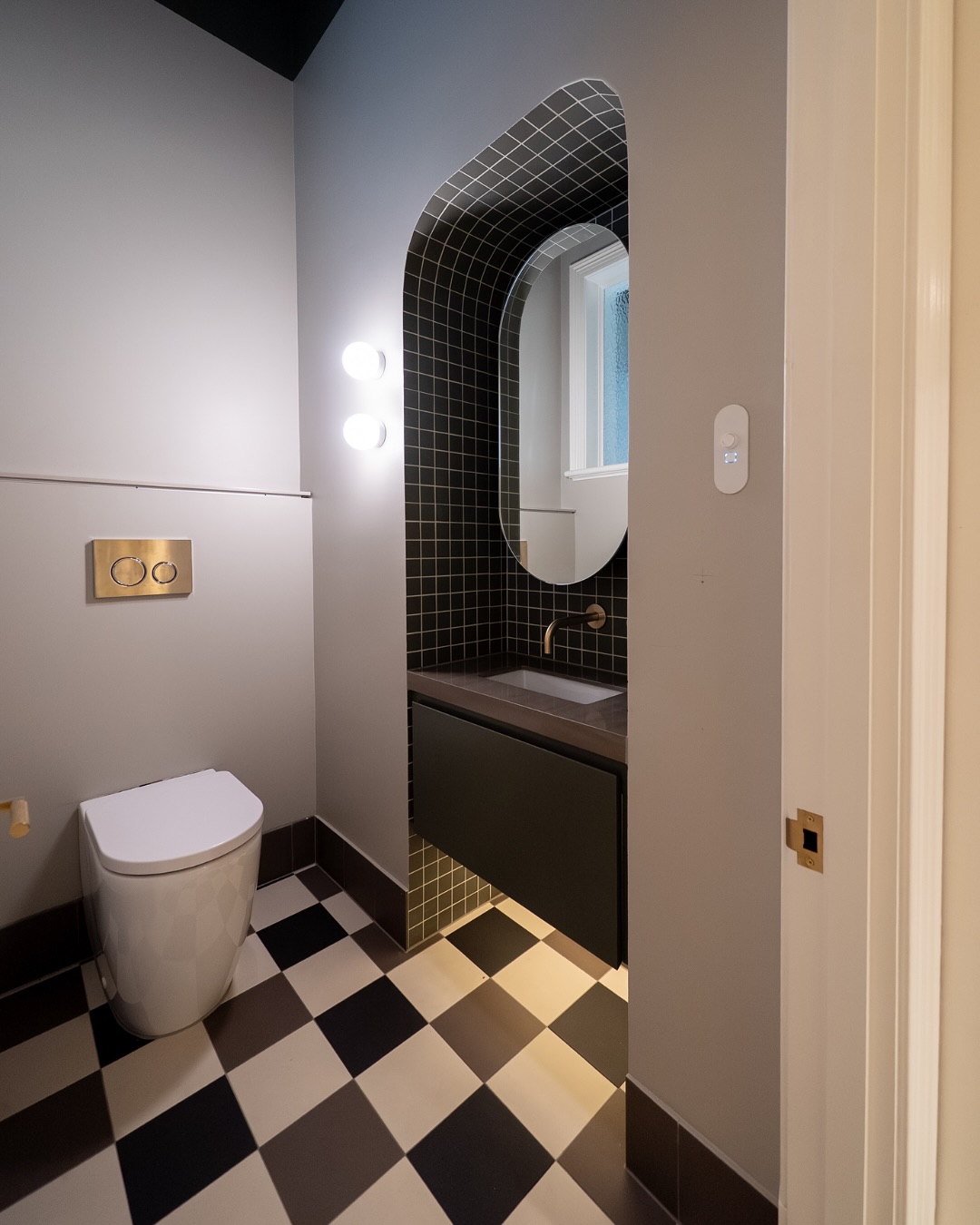 Arched vanity area with black tile feature, round mirror, toilet and checkerboard floor